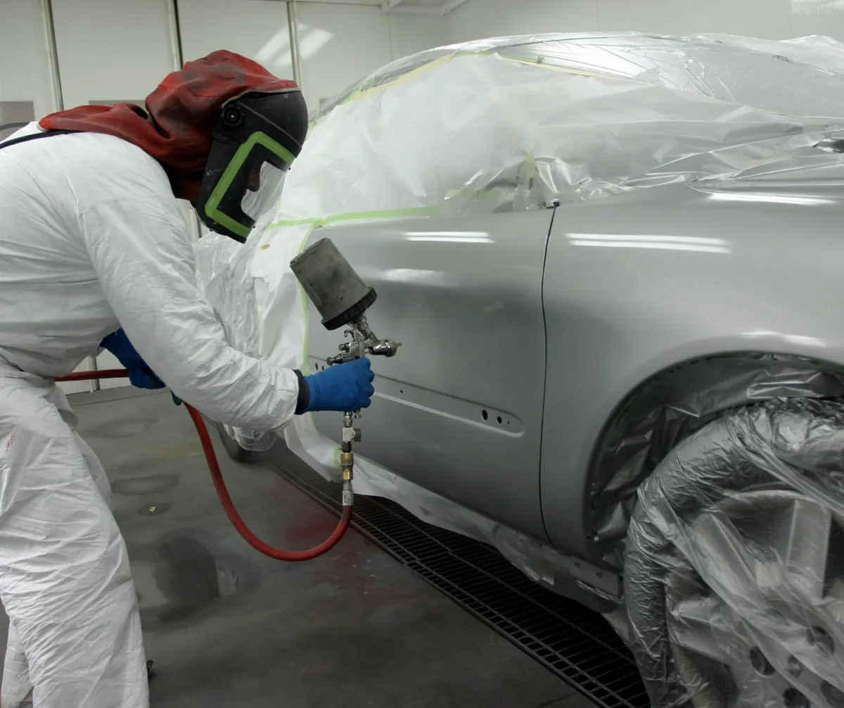 Técnico aplicando pintura automotriz en cabina controlada